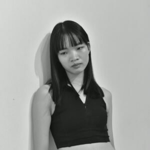 Black and white portrait capturing a thoughtful young woman leaning against a wall.