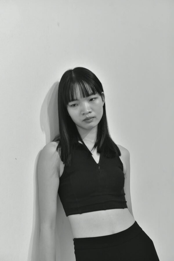 Black and white portrait capturing a thoughtful young woman leaning against a wall.