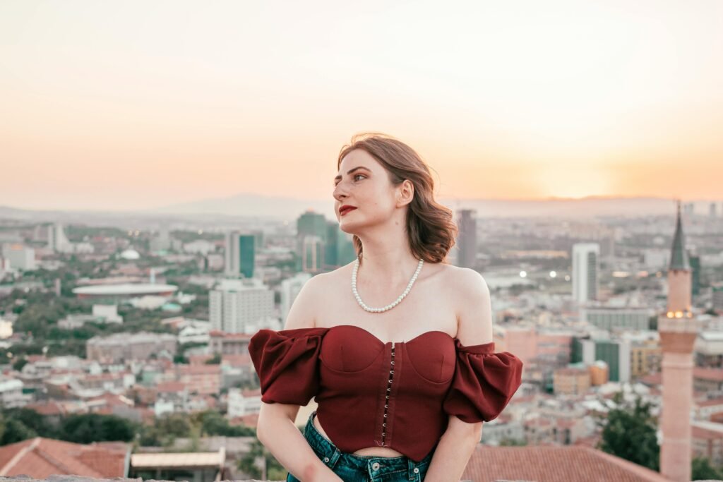 A young woman in stylish attire enjoys a beautiful cityscape view during sunset.
