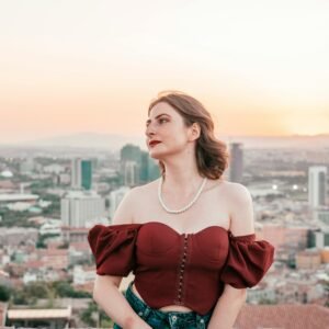 A young woman in stylish attire enjoys a beautiful cityscape view during sunset.